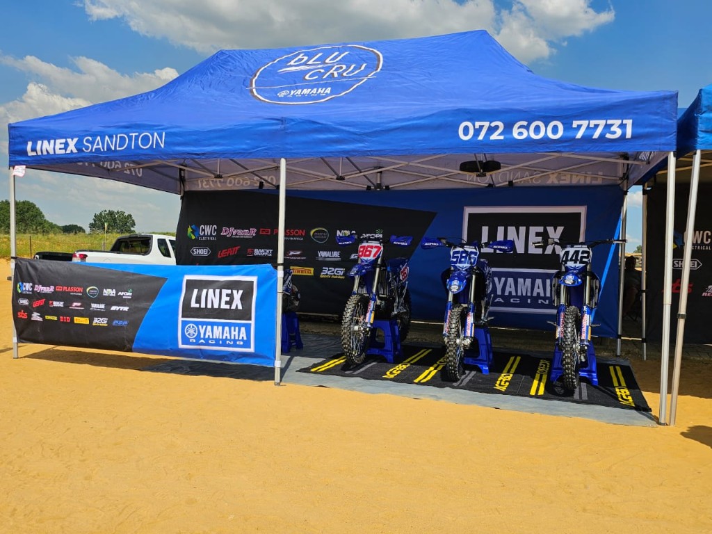 Wide view of Linex Sandton branded gazebo with three Yamaha motocross bikes and contact details by Plan Photo Repro